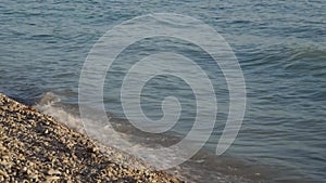 waves break on a pebble beach at sunset.