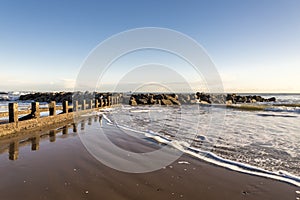 Waves break through a scenic small breakwater structure at Aberdeen city beach in a beautiful sunny day, Scotland