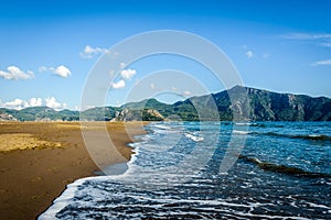 Waves breaking and forming sea foams on a sandy beach under clea