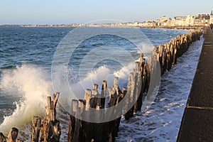 Waves are breaking on the logs of breakwaters on the embankment in Saint-Malo