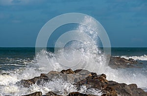 Waves breaking over a rock jetty wall.