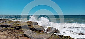 Waves breaking on the rocks on the beach with the sea and blue sky in the background photo
