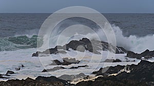 Waves breaking on the rocky coast of Vancouver Island viewed from Wild Pacific Trail in Ucluelet, Canada with foam in water.