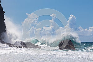 Waves, breaking on rocky, pristine shoreline under blue sky with