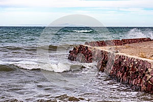 Waves breaking at rustic tourist viewpoint with red stone wall