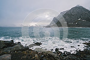 Waves are breaking on the shore and foaming dark blue turquoise sea water on the shoreline under cloudy rainy sky