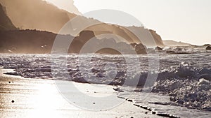 Waves breaking on the shore of a Tenerife beach with back light of the oncoming sunset