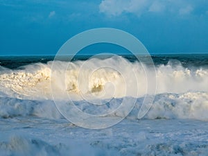 waves coming in the surf on the beach at sunset, with a lighthouse visible on