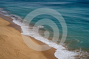 Waves crash along the sandy, expansive beach in Armacao de Pera, Portugal in the Algarve during winter. Footprints in sand