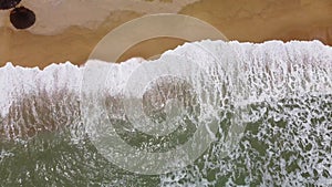 The waves crash onto the beach from a bird's eye view.