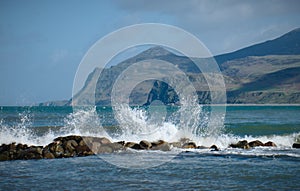 Waves crash on sea defense with a hilly peninsula in North Wales