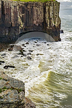 Waves crashing against a cliff and a cave on the coast