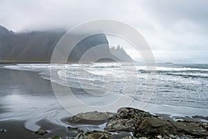 Waves are crashing ashore on Stokksnes peninsula black beach with vestrahorn mountain chain in the background.