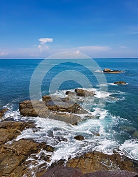 Waves crashing on the black rocks beneath a blue sky at Koh Kham Tok Island Ranong Province, Thailand. Andaman sea