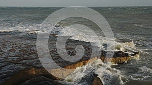 Waves crashing on the cliffy shoreline in Portland, England, on a clou