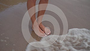 Waves crashing on female feet standing on a sandy beach