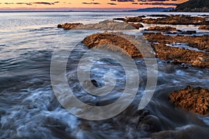 Waves crashing over rocks on the jagged coastline of Waiheke Island, New Zealand taken on a long exposure to smooth out the water