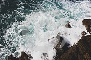 Waves crashing on rocks, Atlantic Ocean. Azure sea waves with white foam breaking on coast. Splash of aquamarine sea water.