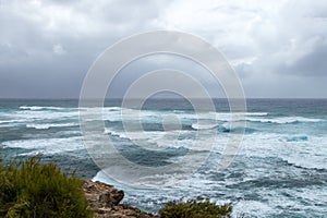 Waves crashing on the rocky coastline with dark ominous clouds photo