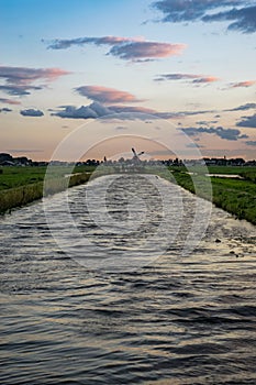 Waves in a dutch canal with a beautiful perspective. A distant windmill stands at the end of the canal on the horizon.