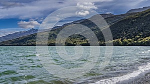 The waves of the emerald lake are foaming on the pebbly shore.