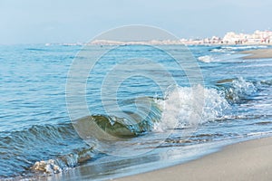 Waves with foam on the sea green color, long sandy beach.