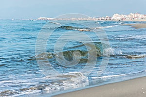 Waves with foam on the sea green color, long sandy beach.