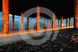 Waves foam under the Bridge, iron columns at the Seashore. Photo of waves on a long Exposure. Evening photo of the sea