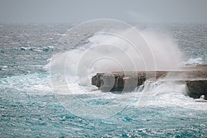 The waves hit the rocks with great splashes. Rocky seashore with blue water, big waves