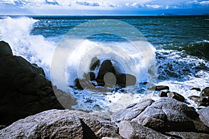 Waves of the Mediterranean Sea which with foam and splashes break against huge stones on the shore, Cagliari, Sardinia