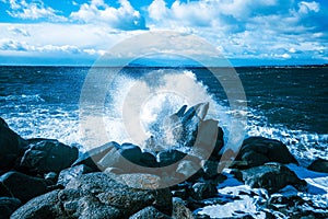 Waves of the Mediterranean Sea which with foam and splashes break against huge stones on the shore, Cagliari, Sardinia