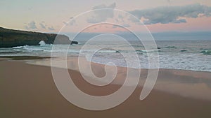 Waves meet tranquil beach at dusk drone view. Sunset cast warm glow over ocean