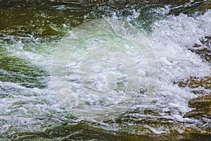 Waves in the mountain river. Fast flow of water_