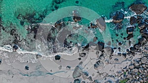 Waves roll on small desolate sand beach with rocks aerial