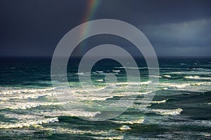 Waves in rough sea with stormy clouds and rainbow