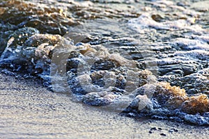 Waves on the sandy shore of a large river. The rays of light are reflected in the waves.