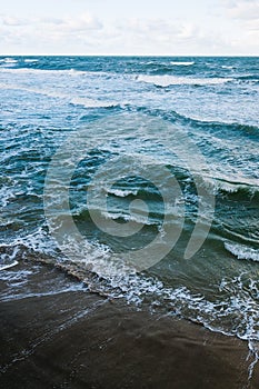 Waves on the sandy shore at sunset background.