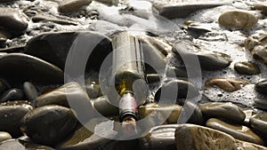 The waves of the sea crash on a bottle with a message lying on the rocks on the shore. An old brown wine bottle closed