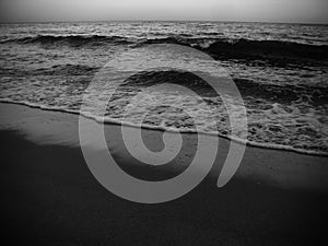 Waves and the sea shore in the evening. Monochrome photo.