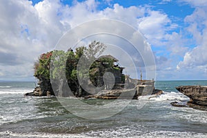 Waves shatter on a cliff at the top of which is the Hindu temple of Tanah Lot. Temple built on a rock in the sea off the coast of
