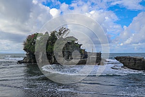 Waves shatter on a cliff at the top of which is the Hindu temple of Tanah Lot. Temple built on a rock in the sea off the coast of