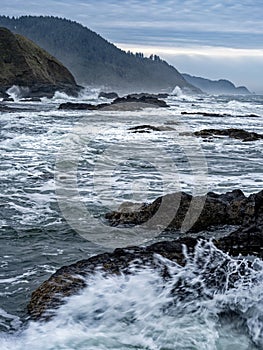 Waves splash against the basalt slabs along the shore of the Pacific Ocean near Florence, Oregon, USA