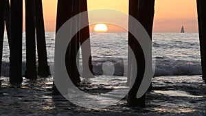 Waves splashing under pier, sunset in Oceanside, California USA. Ocean water, sun and wooden piles.