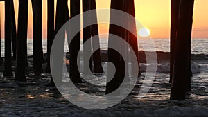Waves splashing under pier, sunset in Oceanside, California USA. Ocean water, sun and wooden piles.