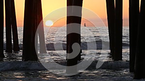 Waves splashing under pier, sunset in Oceanside, California USA. Ocean water, sun and wooden piles.