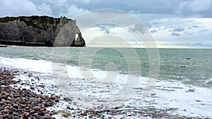 Waves on a stone beach near a rock in cloudy sky backdround