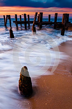 Waves swirl around pier pilings in the Delaware Bay at sunset, s