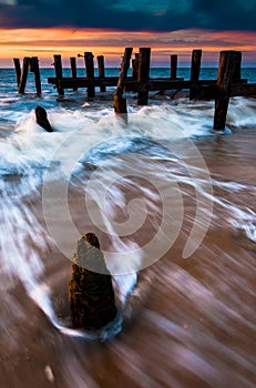 Waves swirl around pier pilings in the Delaware Bay at sunset, s