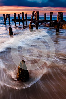 Waves swirl around pier pilings in the Delaware Bay at sunset, s photo