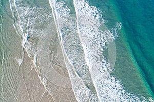 waves of a turquoise sea on the shore of a beach, aerial top drone view